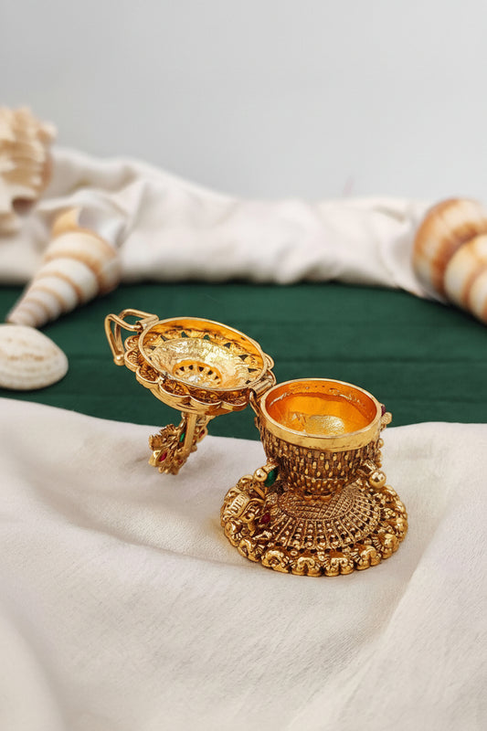 Decorative gold container with intricate designs on a white fabric background